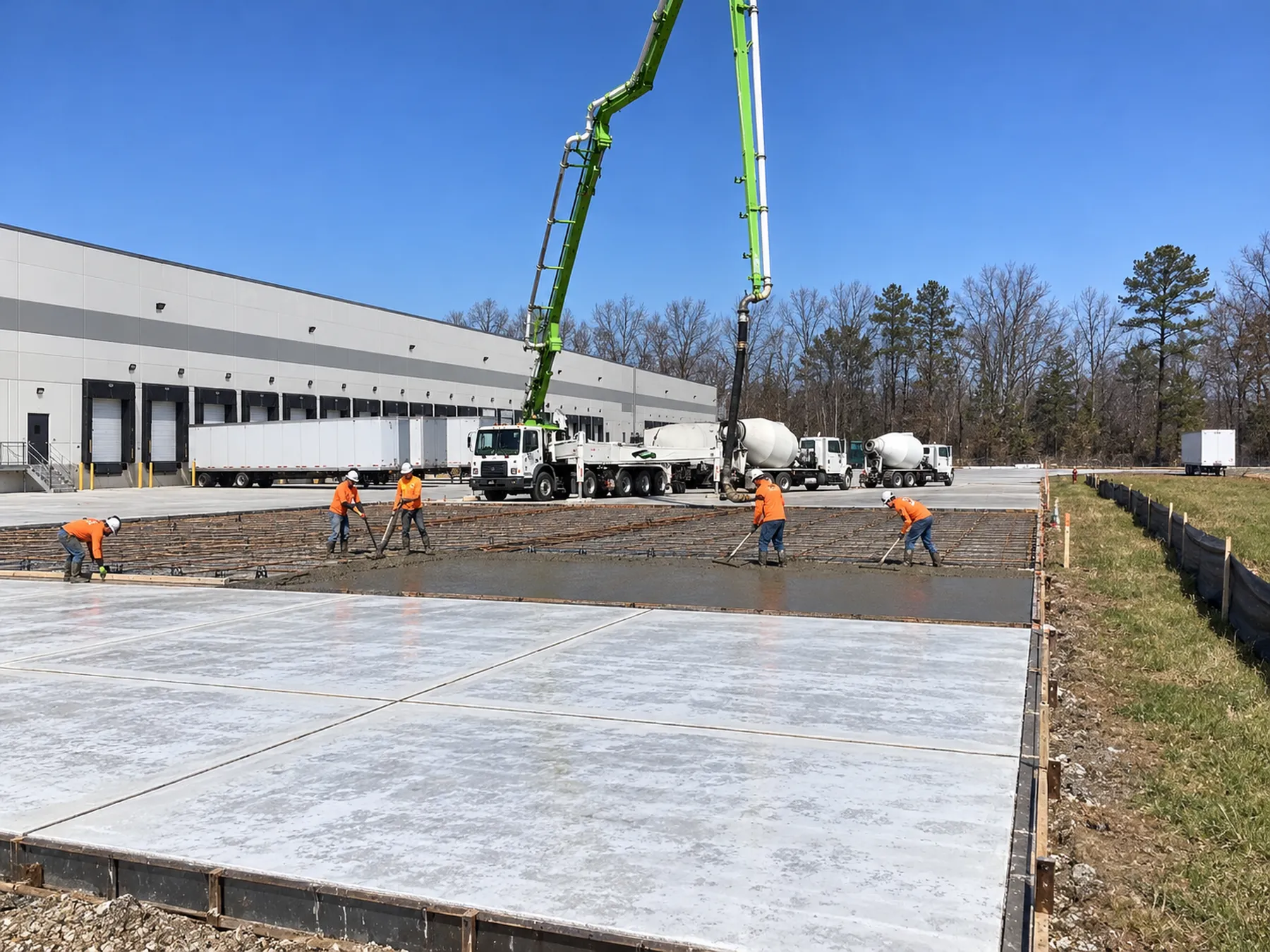 Crew placing concrete over a rebar mat with a pump boom at a distribution center truck court